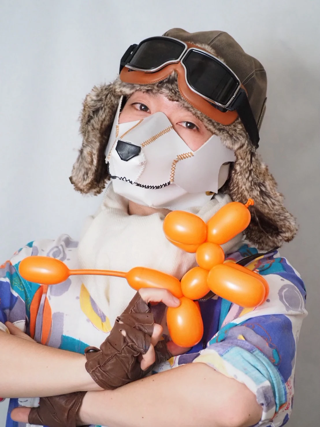 犬のマスクをつけ、オレンジ色のバルーン作品を手にするKey